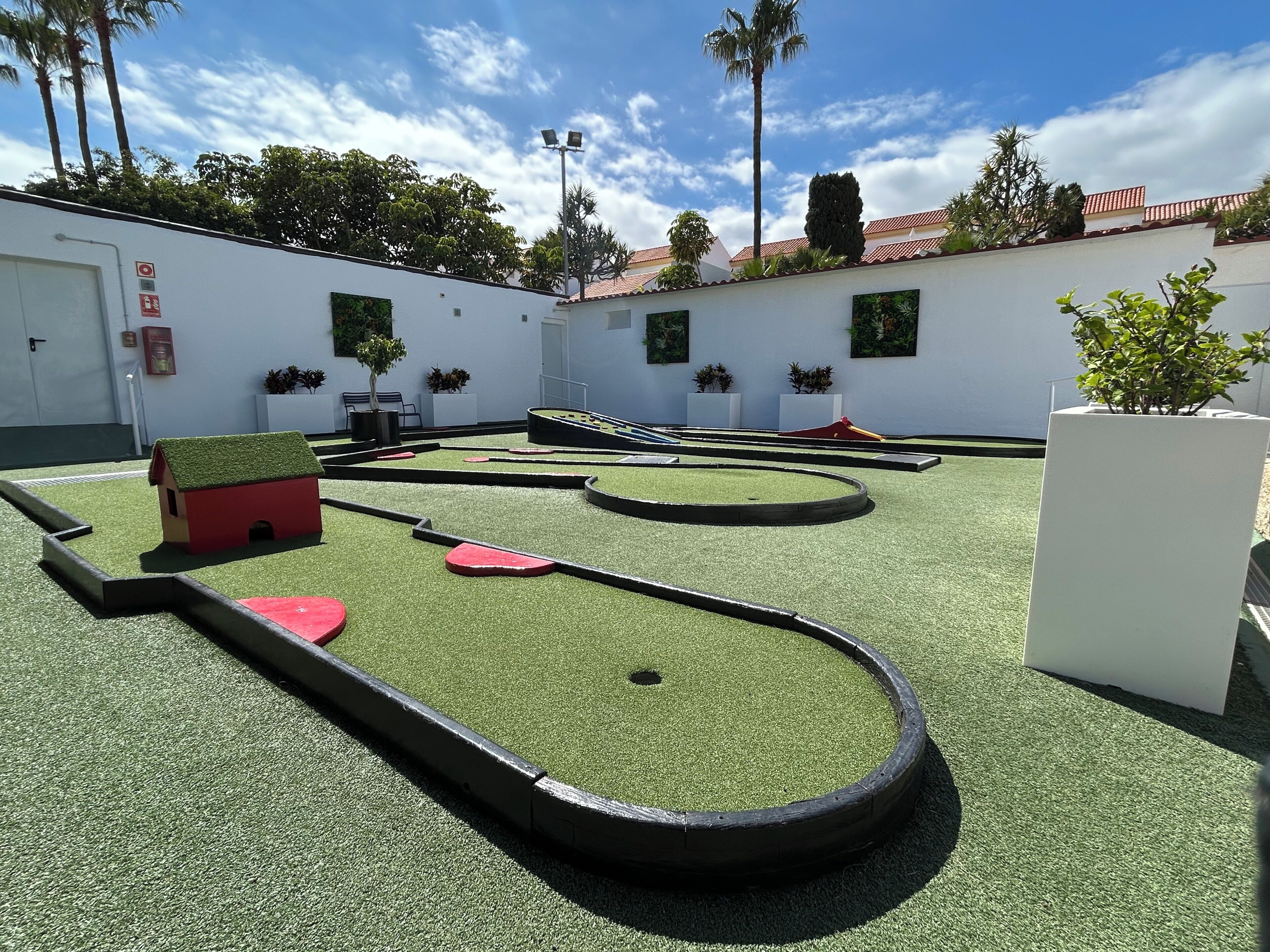 A miniature golf course with a red house, palm trees, and a white building with a red roof.