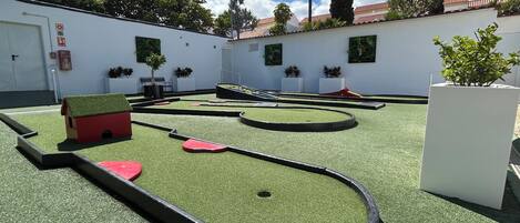 A miniature golf course with a red house, palm trees, and a white building with a red roof.