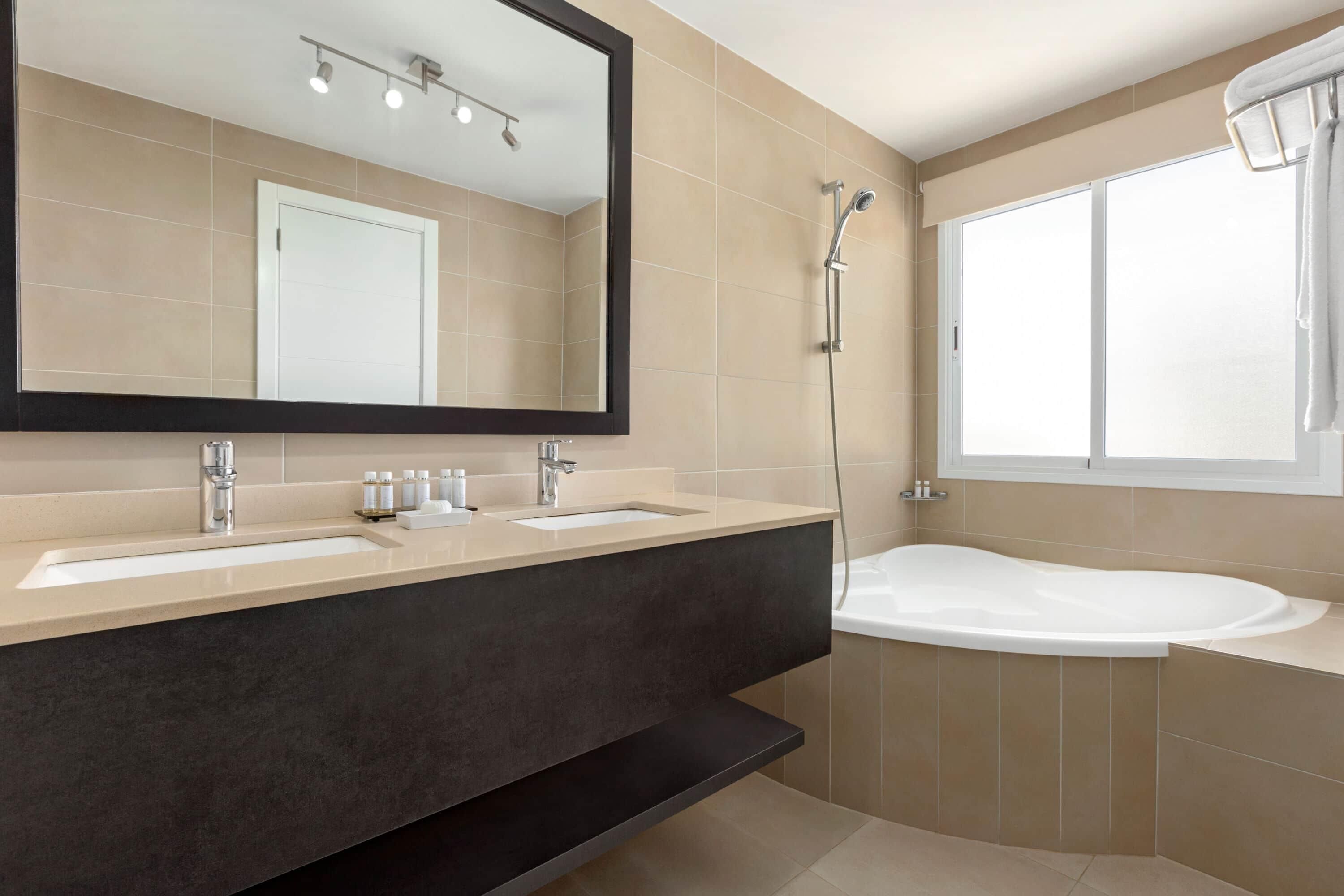 Een moderne badkamer met een wastafel met twee wasbakken, een grote spiegel, een douche en een bad.