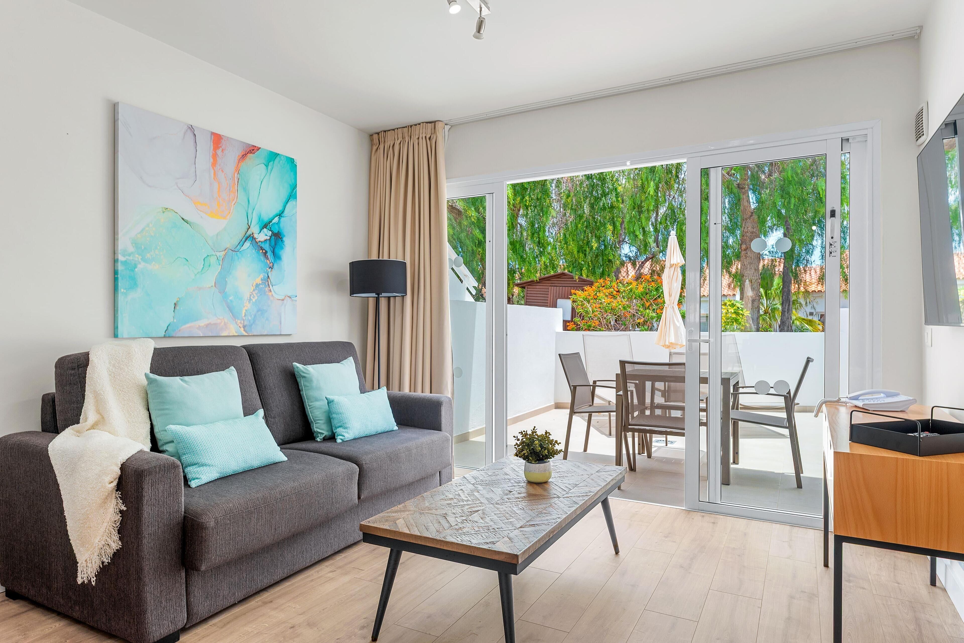 A modern living room with a grey sofa, teal cushions, a coffee table, and a large abstract painting on the wall.
