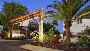 A landscaped entrance with a stone wall, a palm tree, and a building with a sign that reads "WYNDHAM". - Wyndham Residences Golf del Sur (San Miguel de Abona)