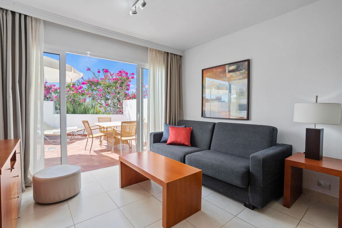 A modern living room with a grey sofa, a wooden coffee table, and a dining area with chairs and a table.