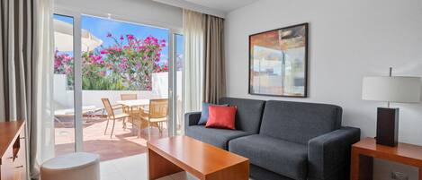A modern living room with a grey sofa, a wooden coffee table, and a dining area with chairs and a table.