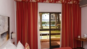 A hotel room with a bed, a table with a kettle, and a view of a pool and outdoor seating. - Praia da Lota Resort - Hotel (Vila Real Santo Antonio)