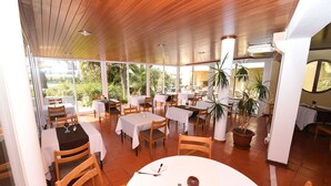 Un restaurant doté de nombreuses tables et chaises, de grandes fenêtres et de plantes en pot.