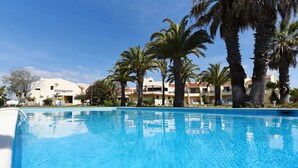 Une piscine à l’eau d’un bleu cristallin, entourée de palmiers et, au fond, un bâtiment avec un toit rouge.