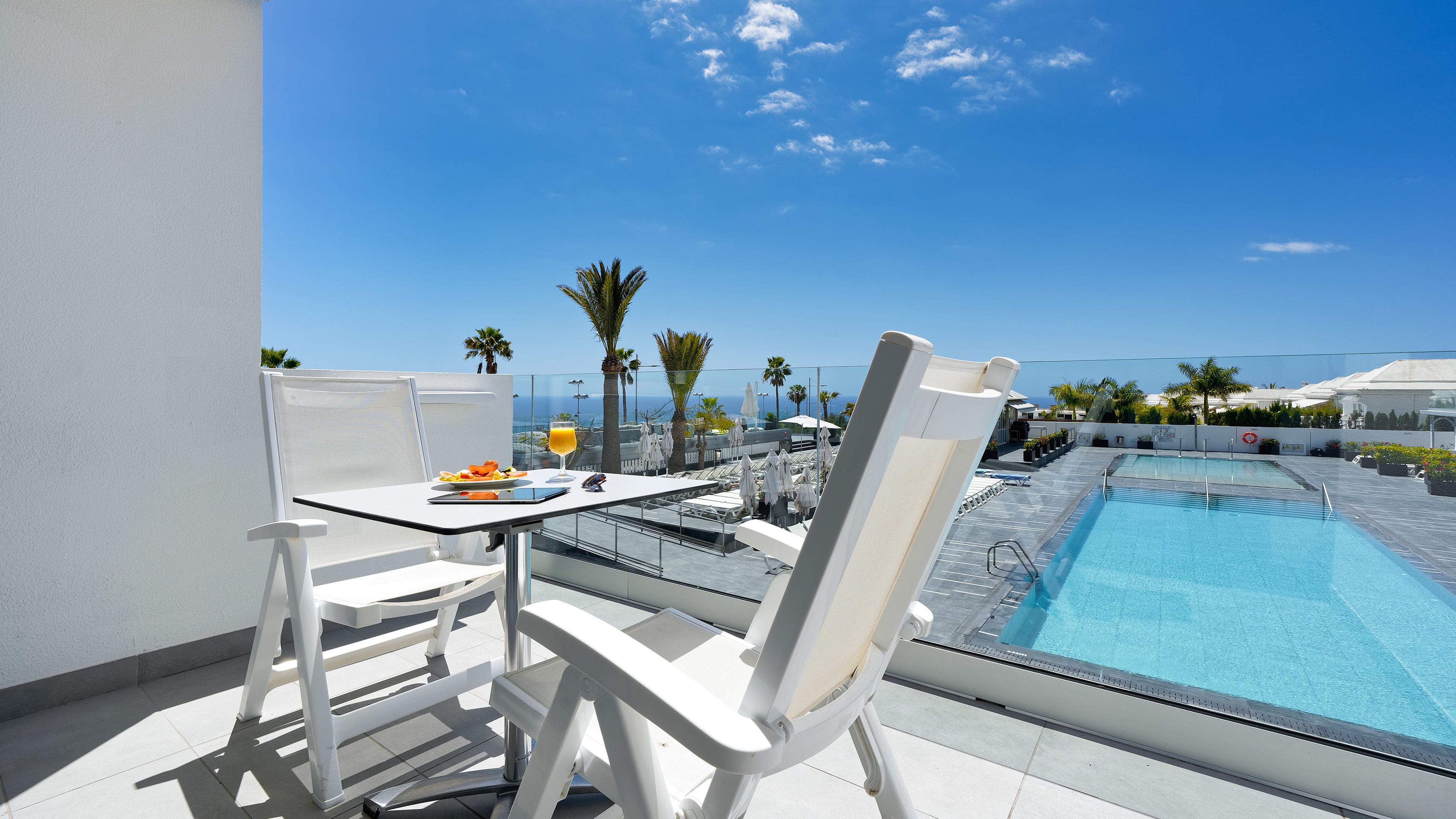 Een balkon met een eettafel, stoelen en een zwembad.