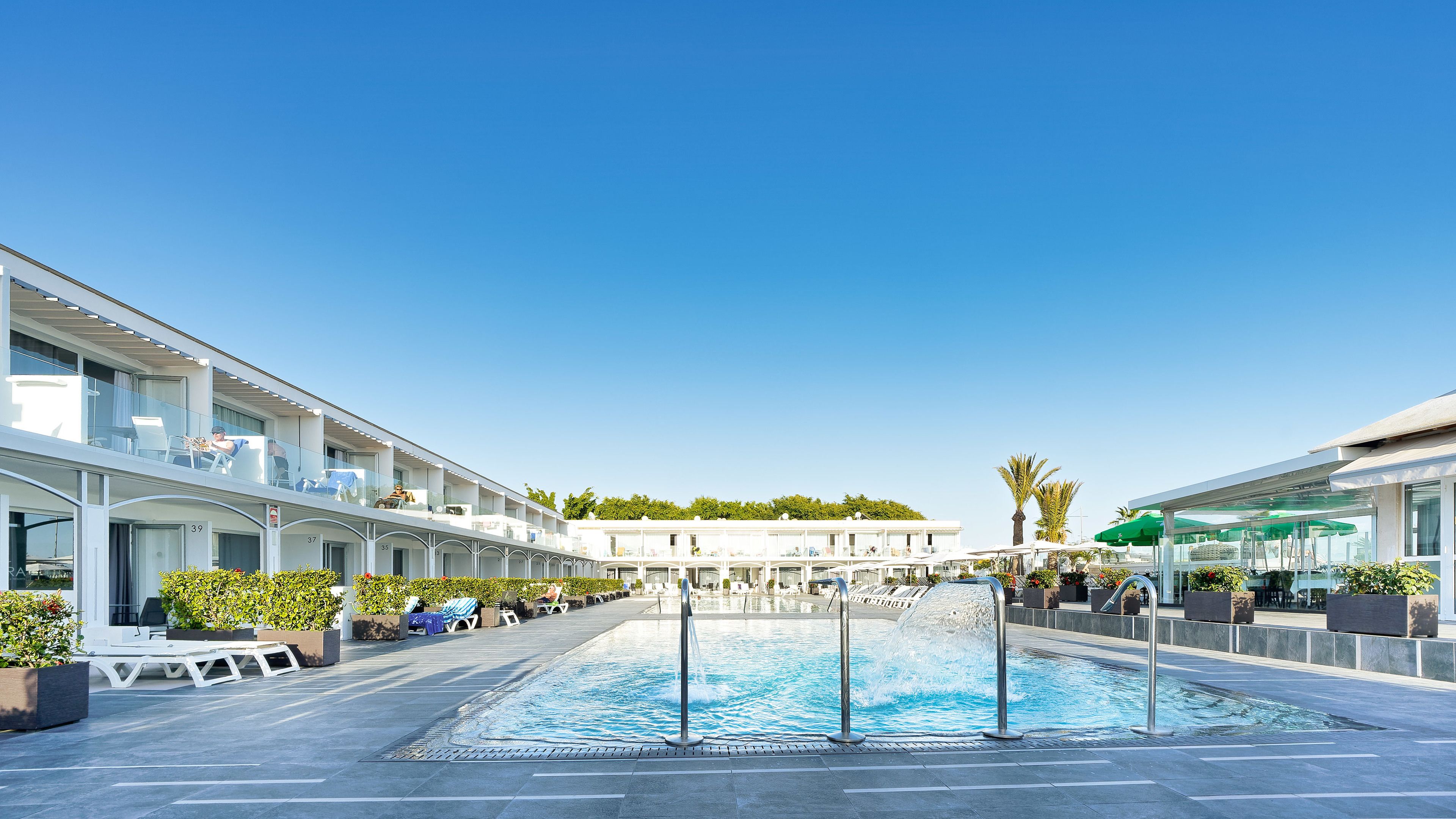 Un hotel con piscina, zona de estar al aire libre y cielo azul despejado.