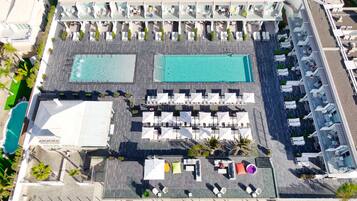 Vista aérea de un hotel con dos piscinas, zonas de estar al aire libre y un bar en la azotea.