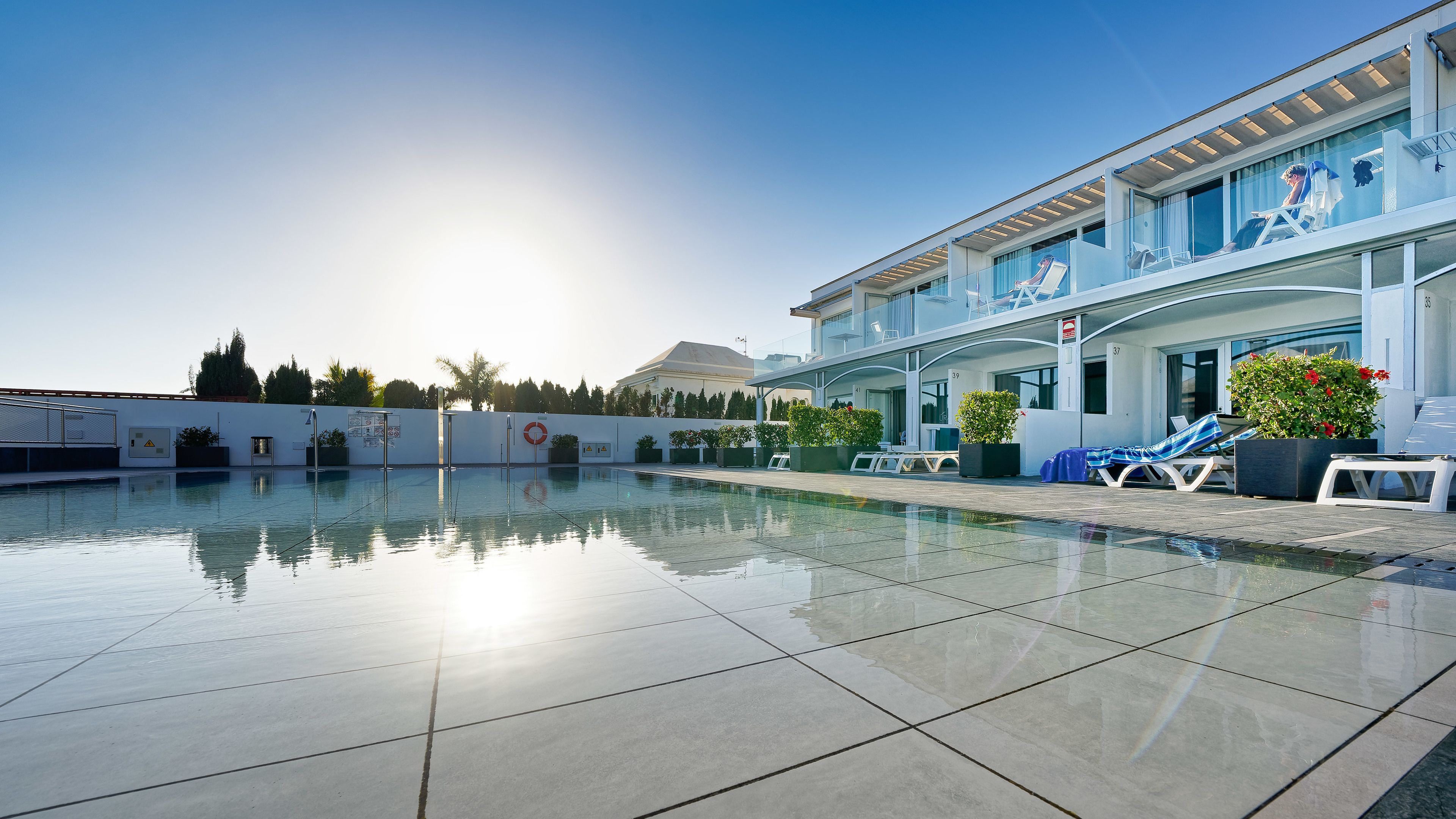 A modern hotel with a swimming pool, sun loungers, and a covered outdoor area.