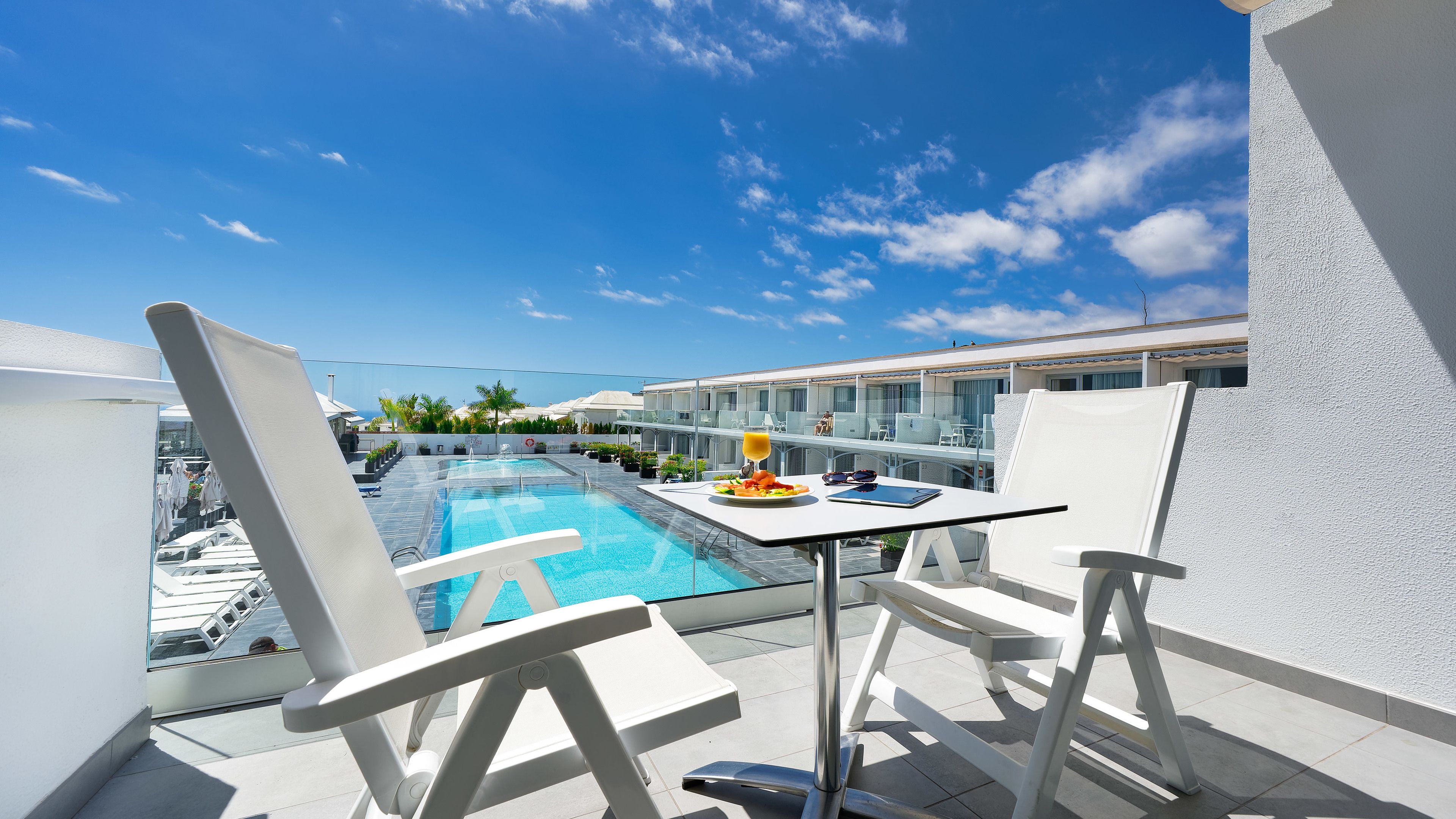 A poolside area with a table, chairs, and a glass of orange juice.