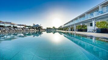 A swimming pool with sun reflecting on the water, lounge chairs, and a building with a balcony.