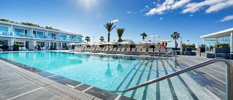 A swimming pool with lounge chairs and umbrellas, surrounded by a modern building with a glass facade.
