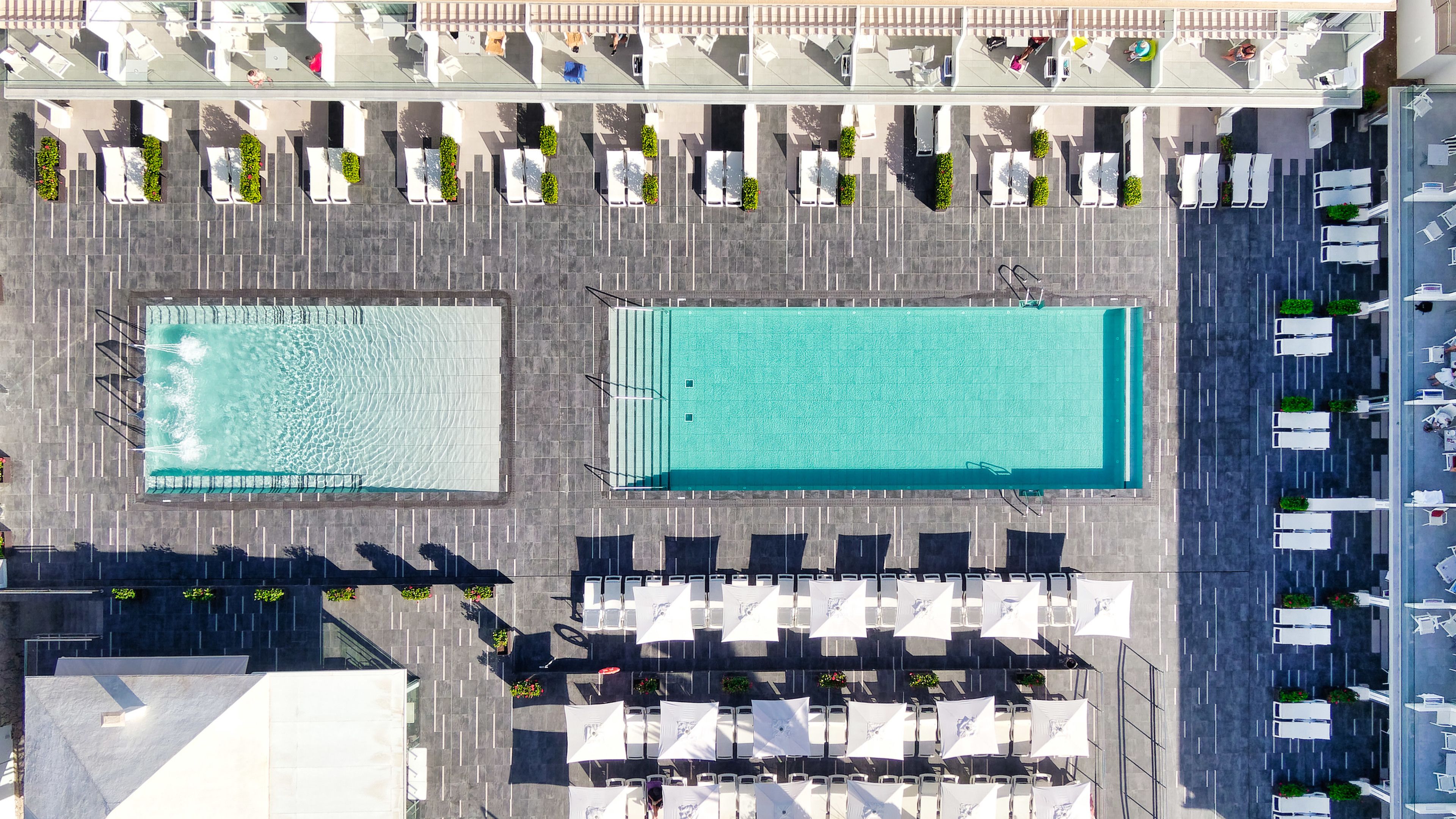 Vista aérea de un hotel con dos piscinas amplias, zonas de estar al aire libre y un estacionamiento.