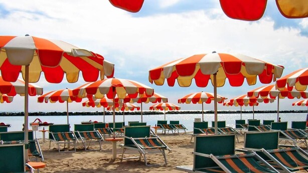Une plage bordée de rangées de chaises longues vertes et de parasols à rayures orange et blanches.