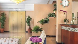 Un hall d’hôtel comprenant un comptoir d’accueil, un canapé agrémenté d’un arrangement floral et des plantes en pot.