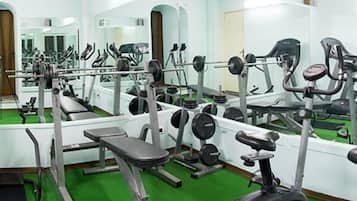 Ein Fitnessstudio mit unterschiedlichen Trainingsgeräten, Spiegeln und einem grünen Teppich.