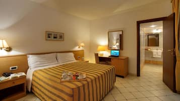 Ein Hotelzimmer mit einem Bett, Nachttischen, einem Schreibtisch mit einem Laptop, einem Spiegel und einem durchgegangenen Türrahmen sichtbaren Badezimmer.