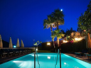 A swimming pool with lounge chairs and umbrellas, surrounded by palm trees and illuminated by ambient lighting. - La Luna (Barano d'Ischia)