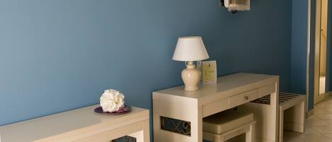 A room with a blue wall, a beige desk with a lamp, and a small white flower on the desk.