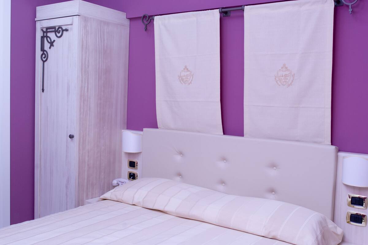 A bedroom with a bed, a wardrobe, and a curtain with a crest.