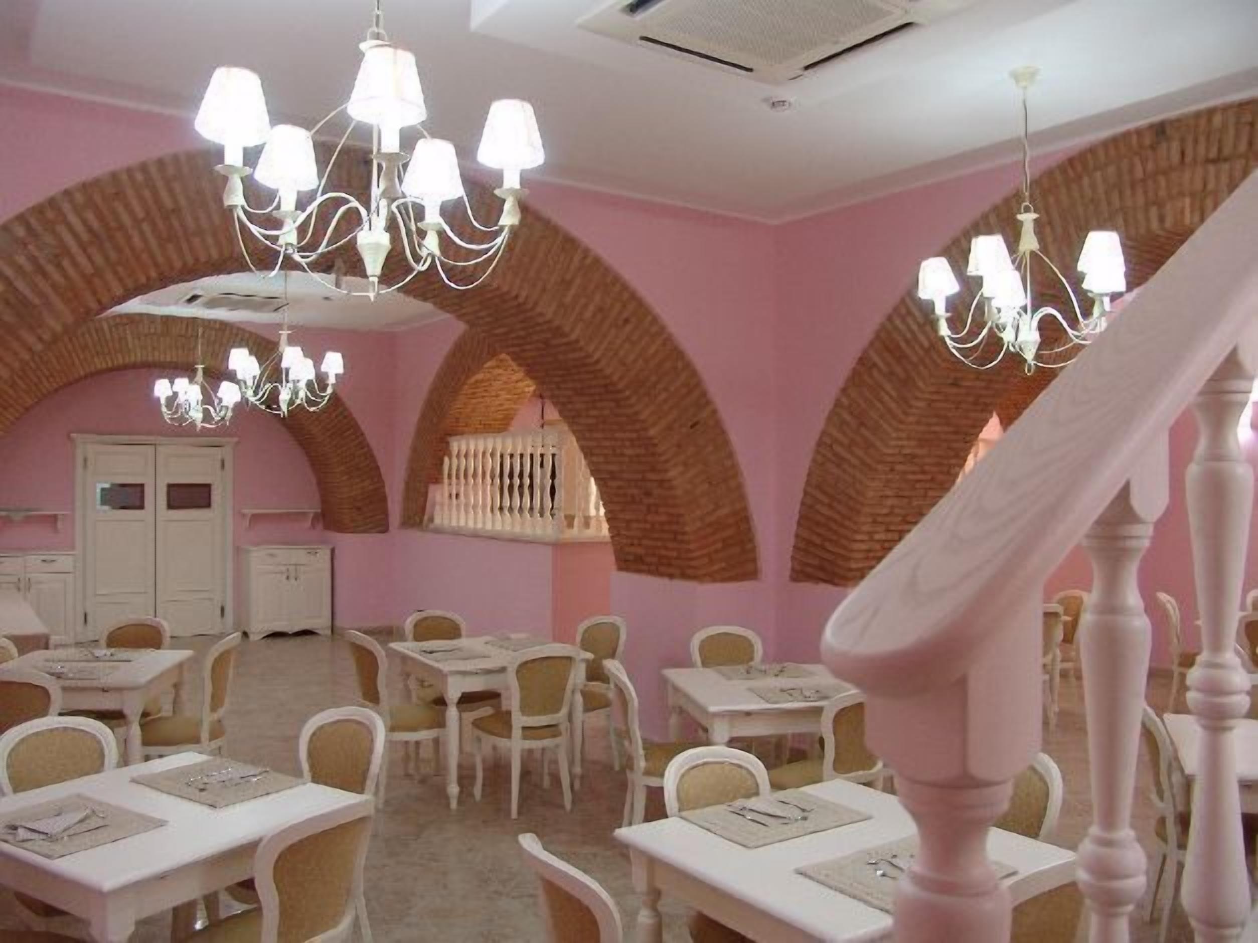 A dining area with pink walls, white tables, and chairs, and a chandelier.