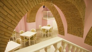 A dining area with white tables and chairs, a pink wall, and a brick archway. - Palazzo Reginella Residence Hotel (Bovalino)