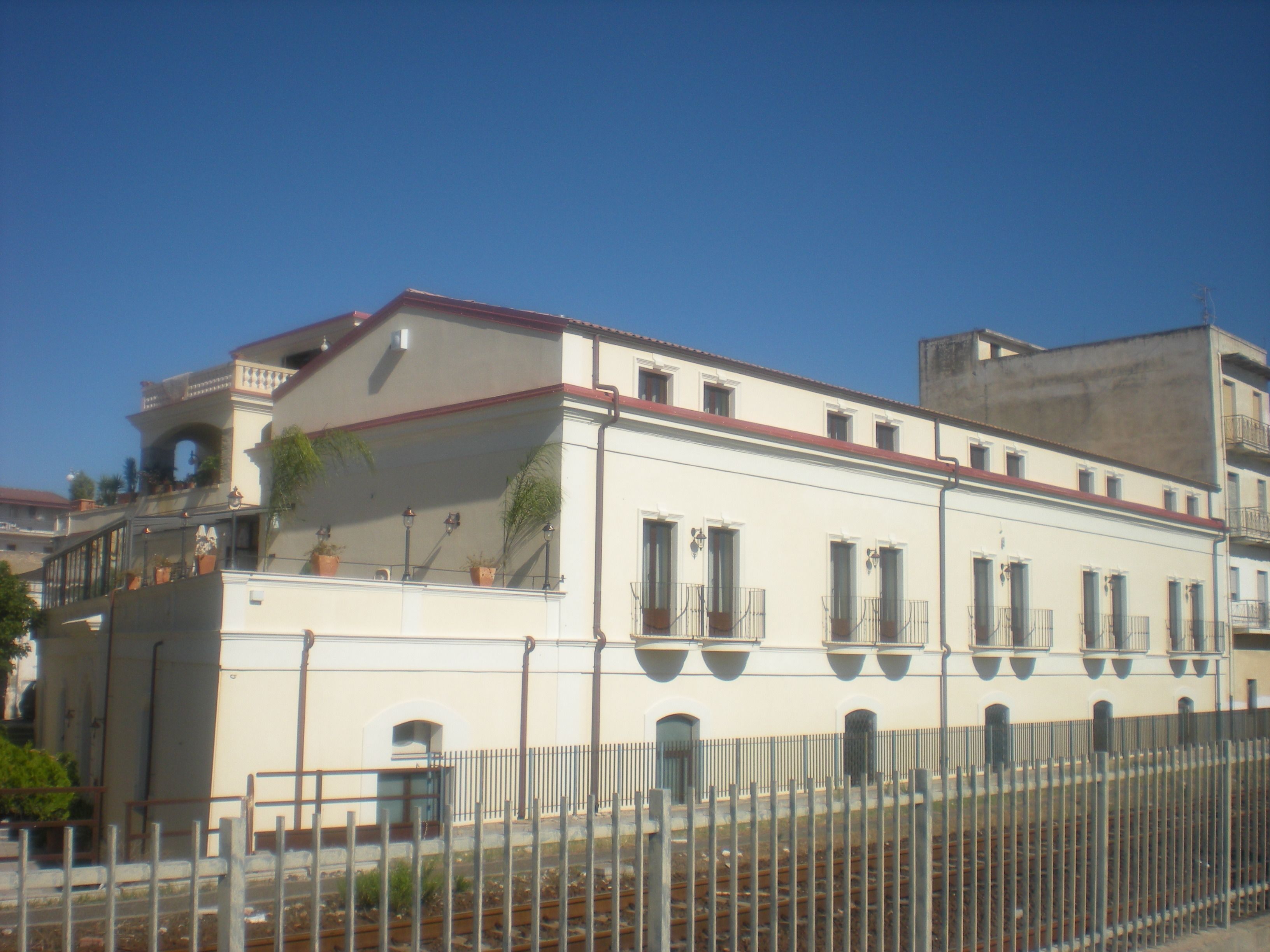 A building with a white facade, multiple windows, and a balcony with potted plants.