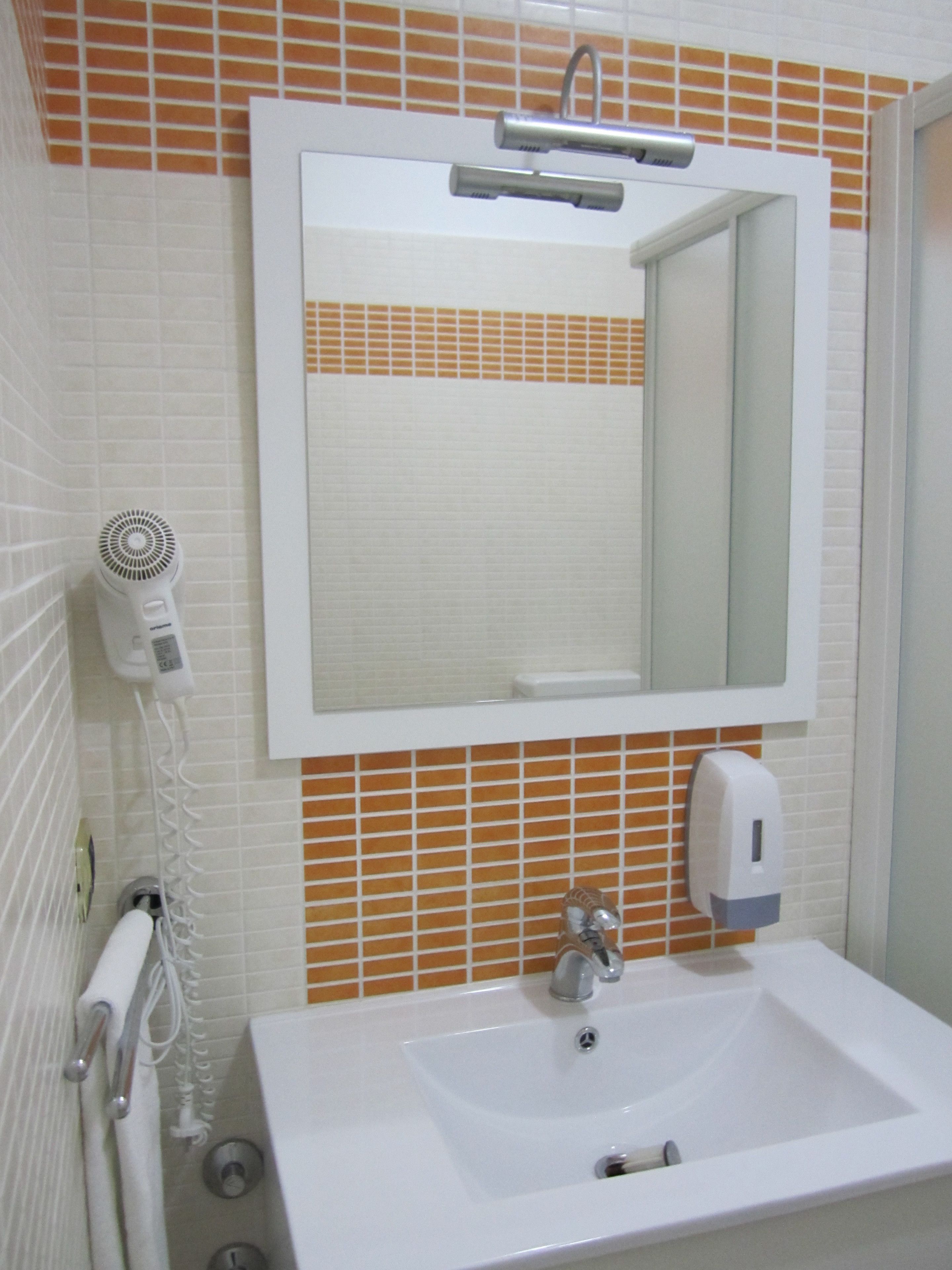 A bathroom with a white sink, a mirror, a hairdryer, and a soap dispenser.