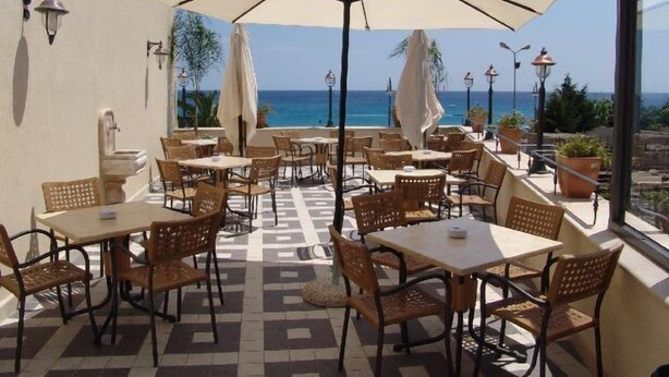 An outdoor patio with tables and chairs, large umbrellas, and a view of the ocean. - Palazzo Reginella Residence Hotel (Bovalino)