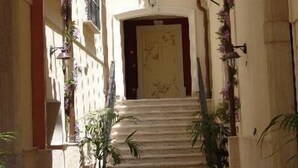 A narrow, sunlit corridor with a staircase leading to a door, flanked by balconies with plants and a hanging light fixture. - Palazzo Reginella Residence Hotel (Bovalino)