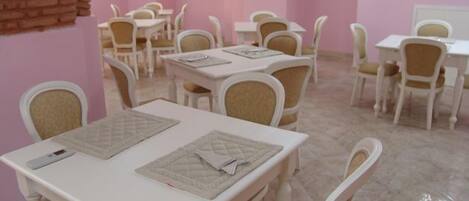 A dining area with white tables and chairs, pink walls, and a brick wall feature.