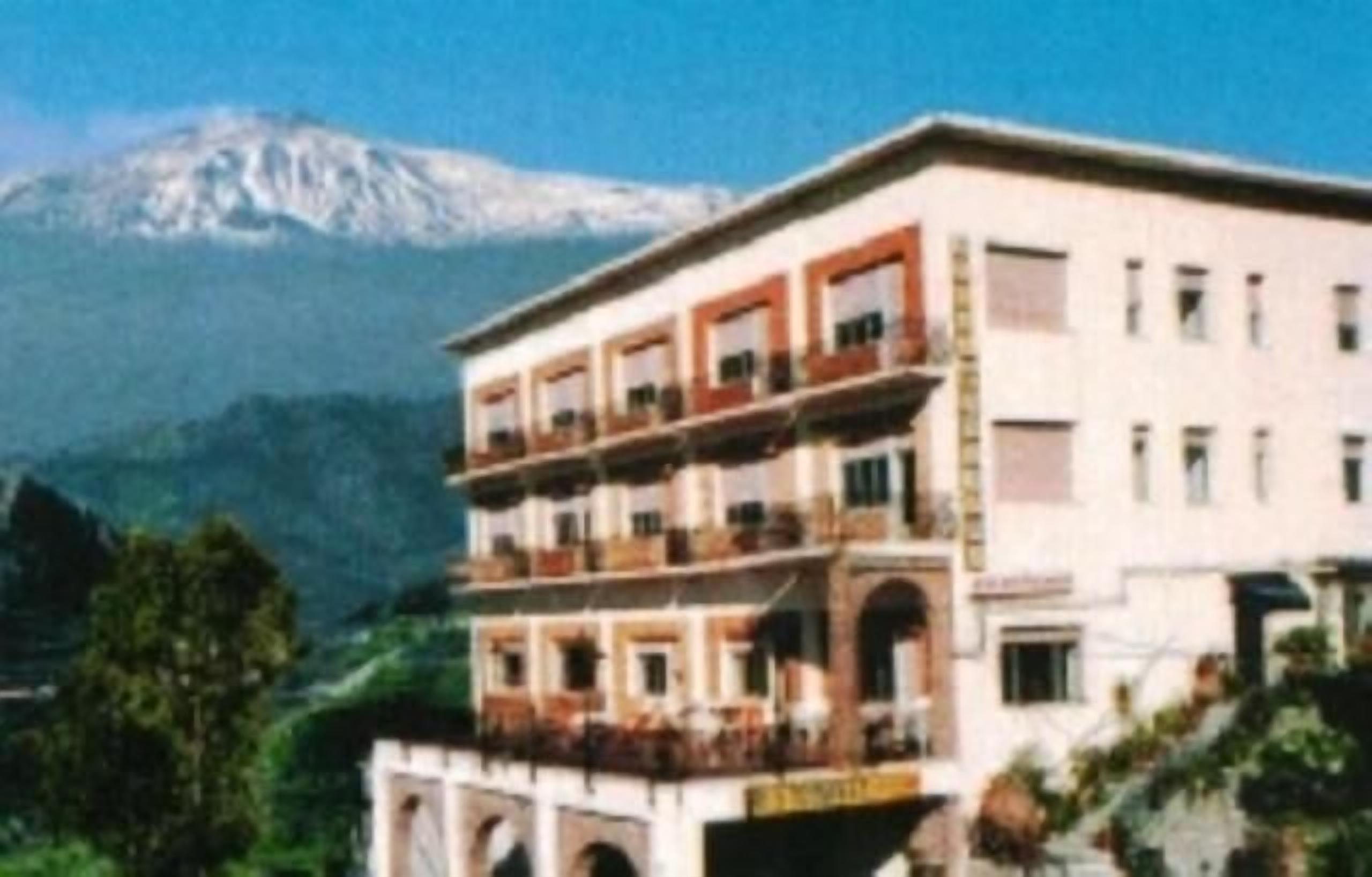 A multi-story building with balconies, set against a mountainous backdrop.