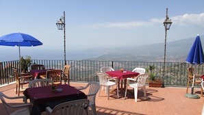 Una terraza al aire libre con mesas y sillas, vistas del paisaje y farolas decorativas.