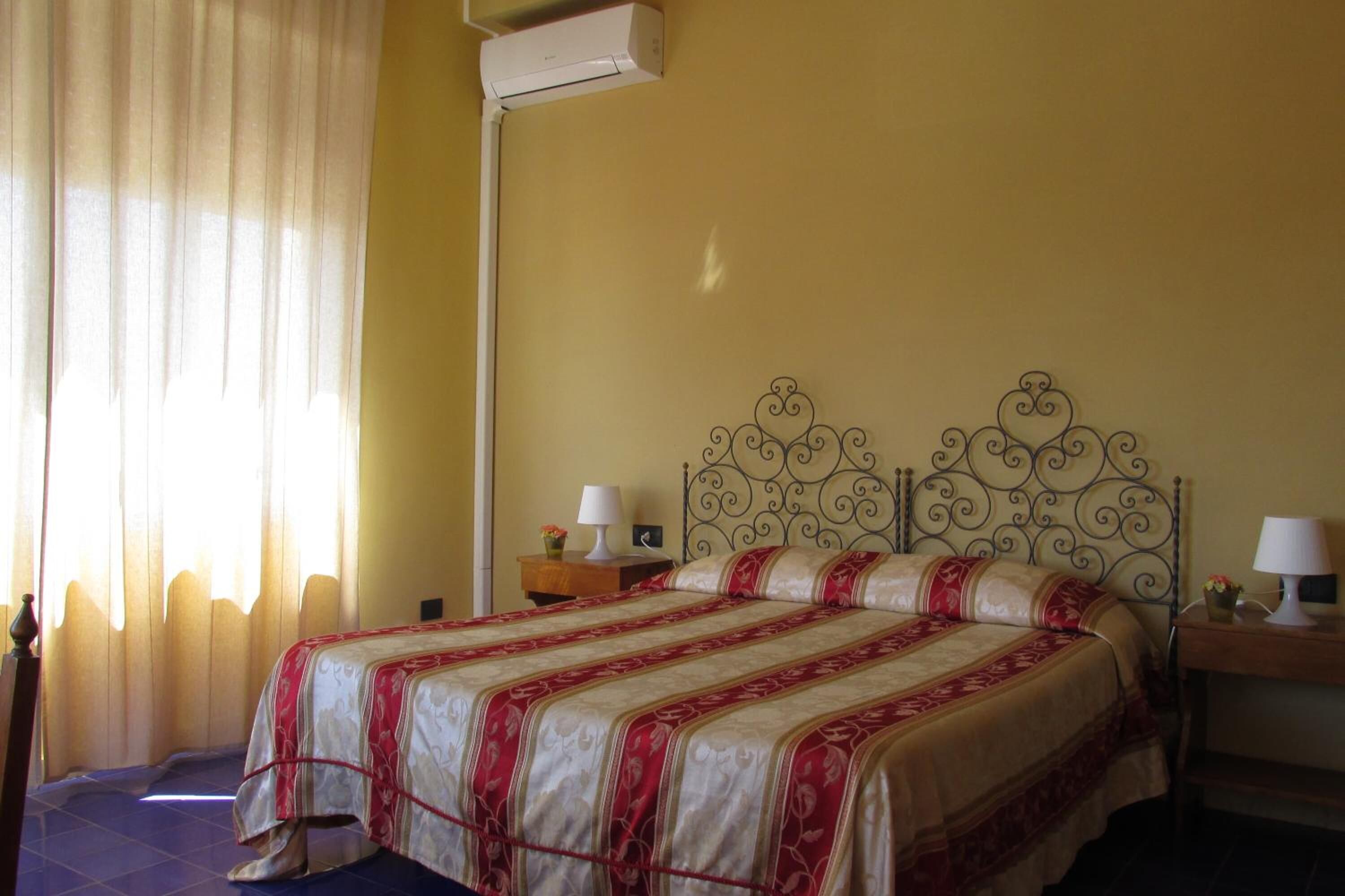 A neatly made bed with a patterned bedspread, a bedside table with a lamp, and a wall-mounted air conditioner.