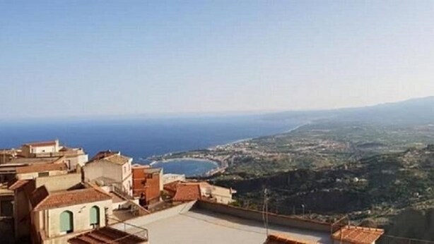 Un paysage urbain côtier avec des bâtiments situés sur une colline surplombant la mer et une montagne lointaine.