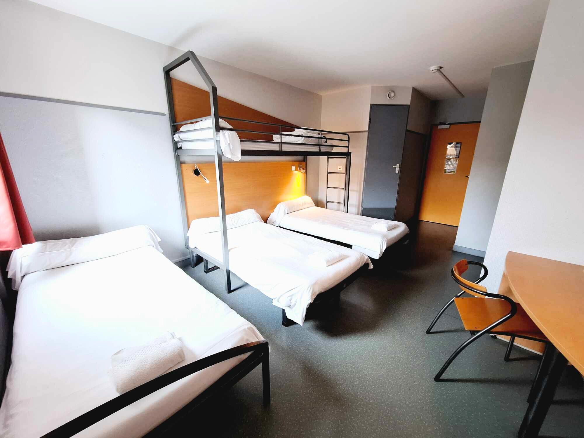 Habitación de hotel con literas, un escritorio y una silla.