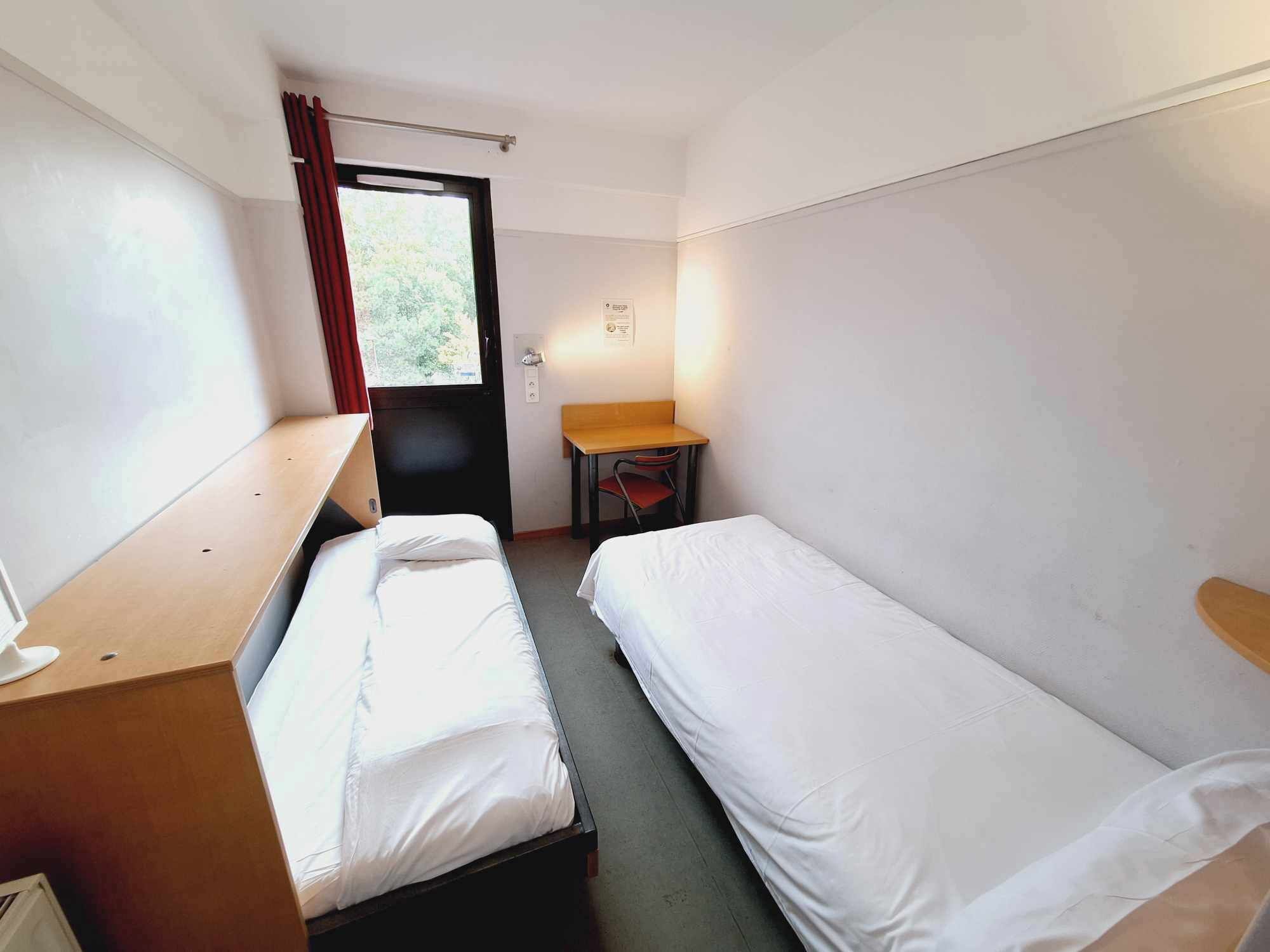 Una habitación pequeña y sencilla con dos camas individuales, un escritorio y una silla.