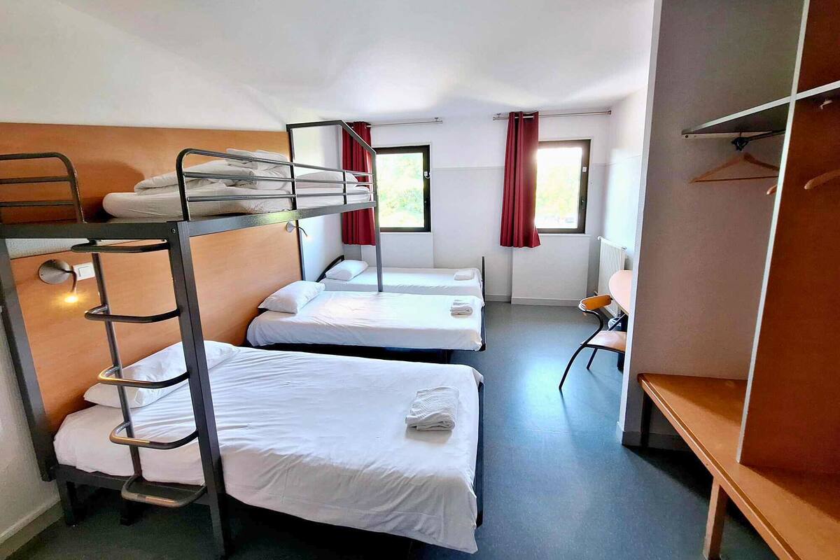 A dormitory room with bunk beds, a single bed, a desk, and a chair.