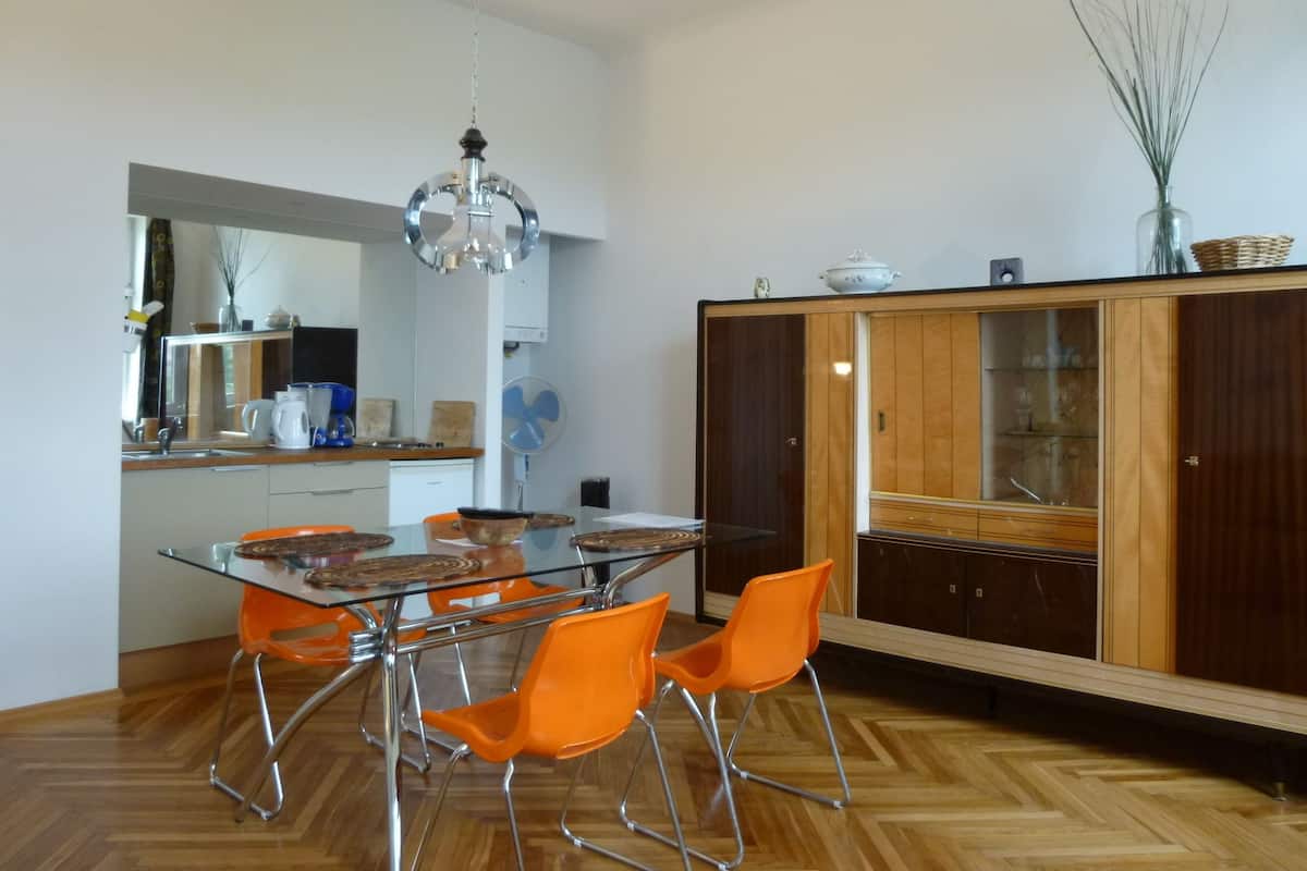 A modern kitchen with a dining table, orange chairs, and a wooden cabinet with glass doors.