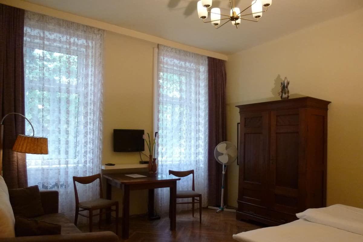 A hotel room with a bed, a desk with a chair, a TV, a cabinet, and a standing fan.