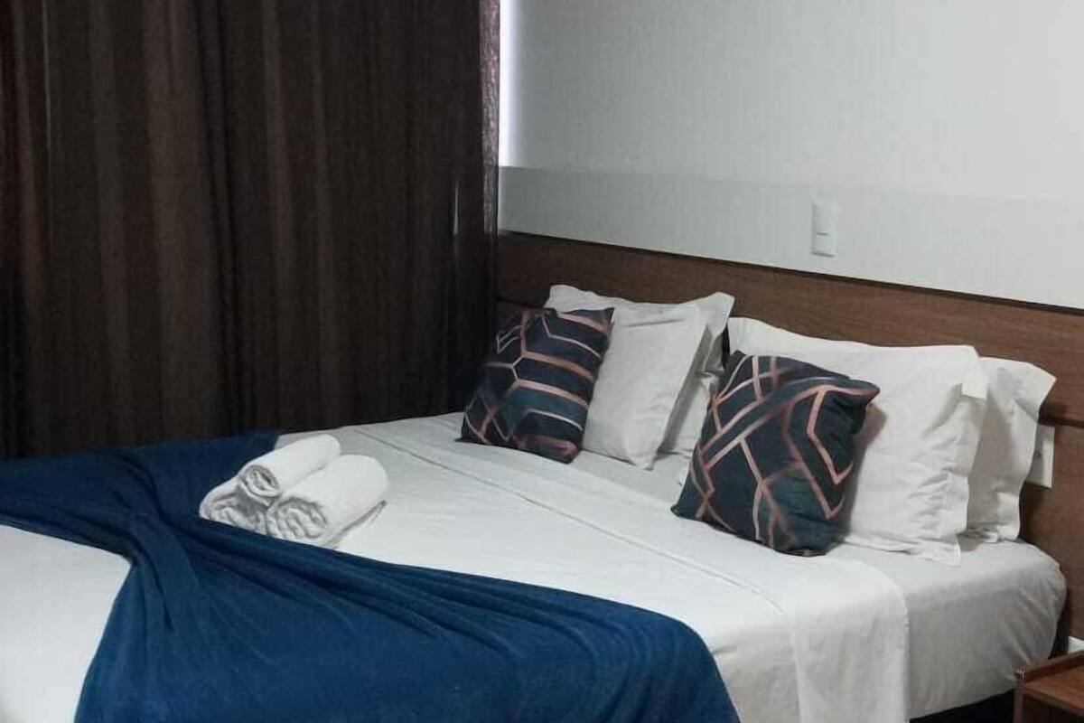 A hotel room with a bed, dark curtains, a white headboard, and a tiled floor.