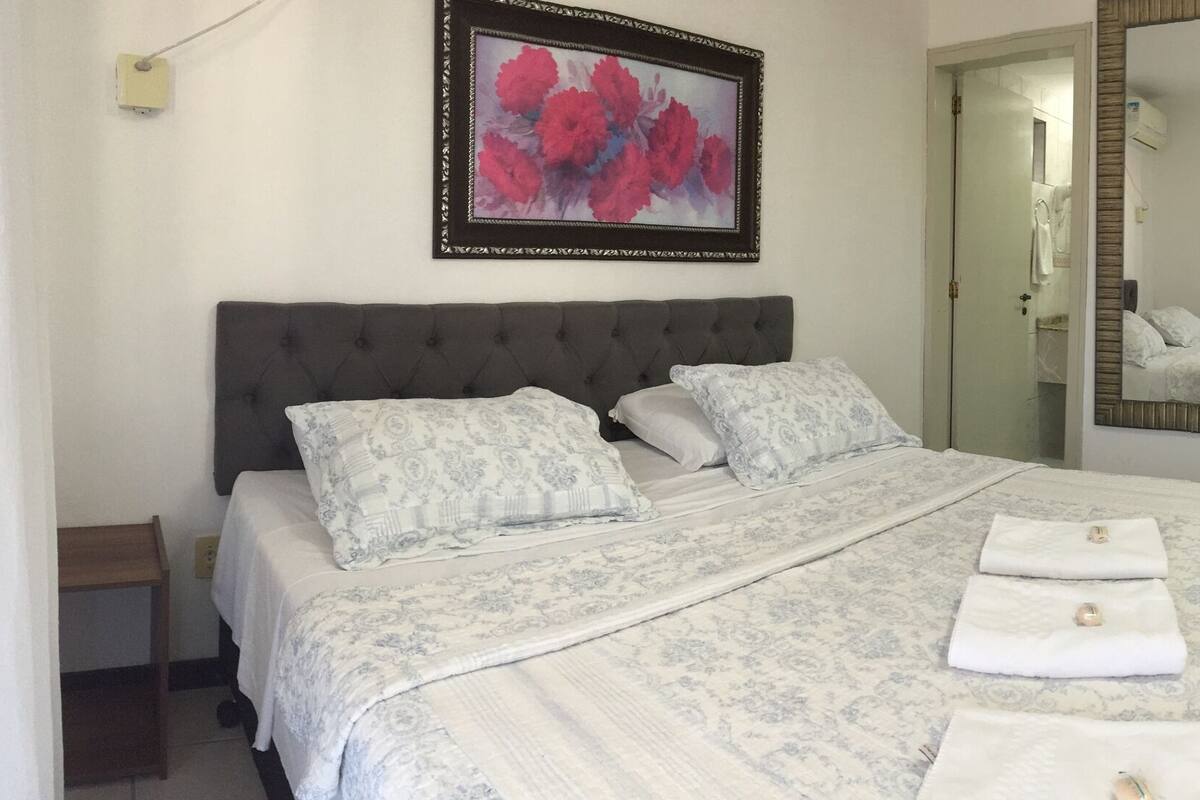 A hotel room with a large bed, a bedside table, a wardrobe, and a small desk with a chair.
