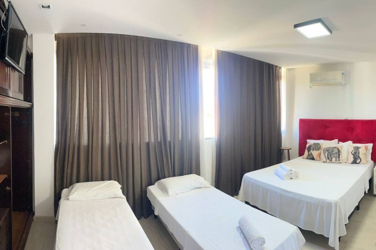 A hotel room with two single beds, a red headboard, a wardrobe, and a flat-screen TV.