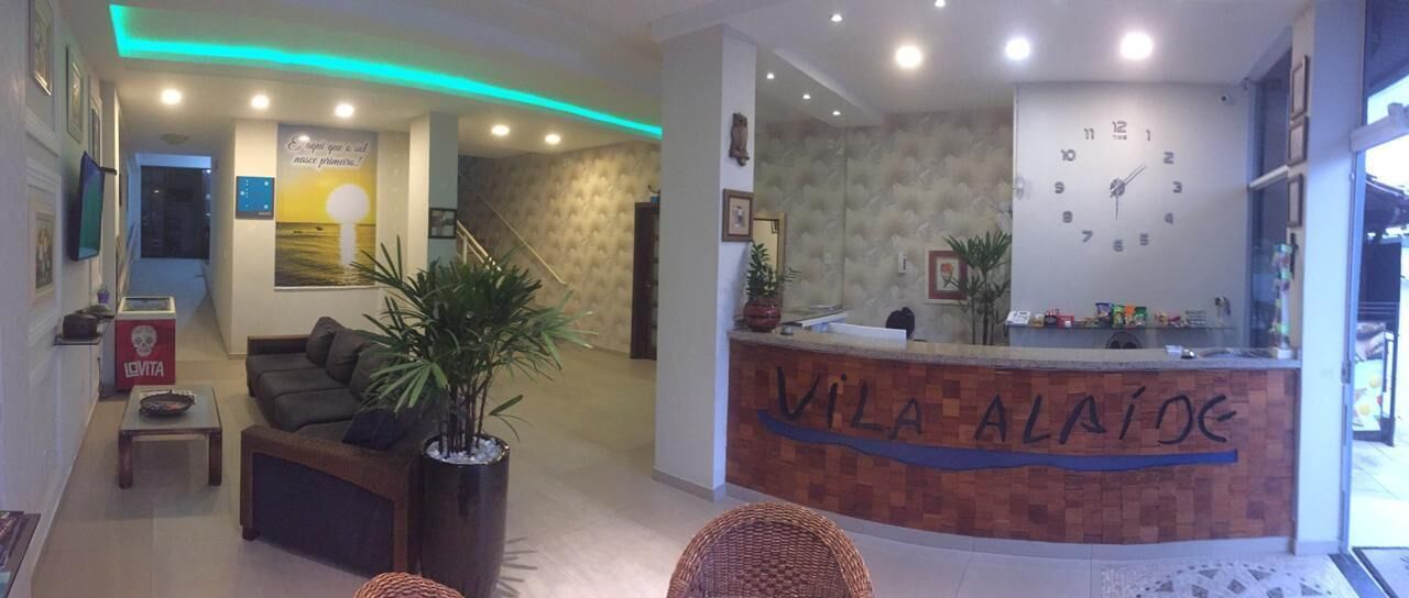 A reception area with a reception desk labeled "VILA ALAIÓ," a sofa, a small table, and a potted plant.