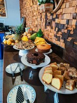 Mesa de buffet com diversos alimentos, incluindo bolos, pães e frutas.