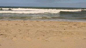 Una playa con olas, orilla arenosa y cielo parcialmente nublado.