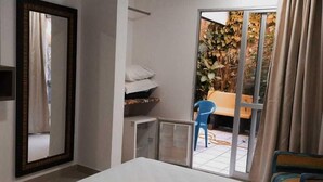 Habitación de hotel con una cama, un espejo, una puerta corrediza de vidrio a un espacio exterior con plantas y una silla azul.