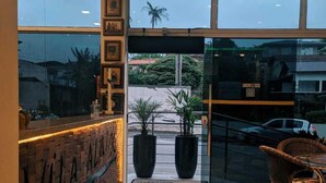Un hall de hotel con una recepción, plantas en macetas y vistas a la calle.