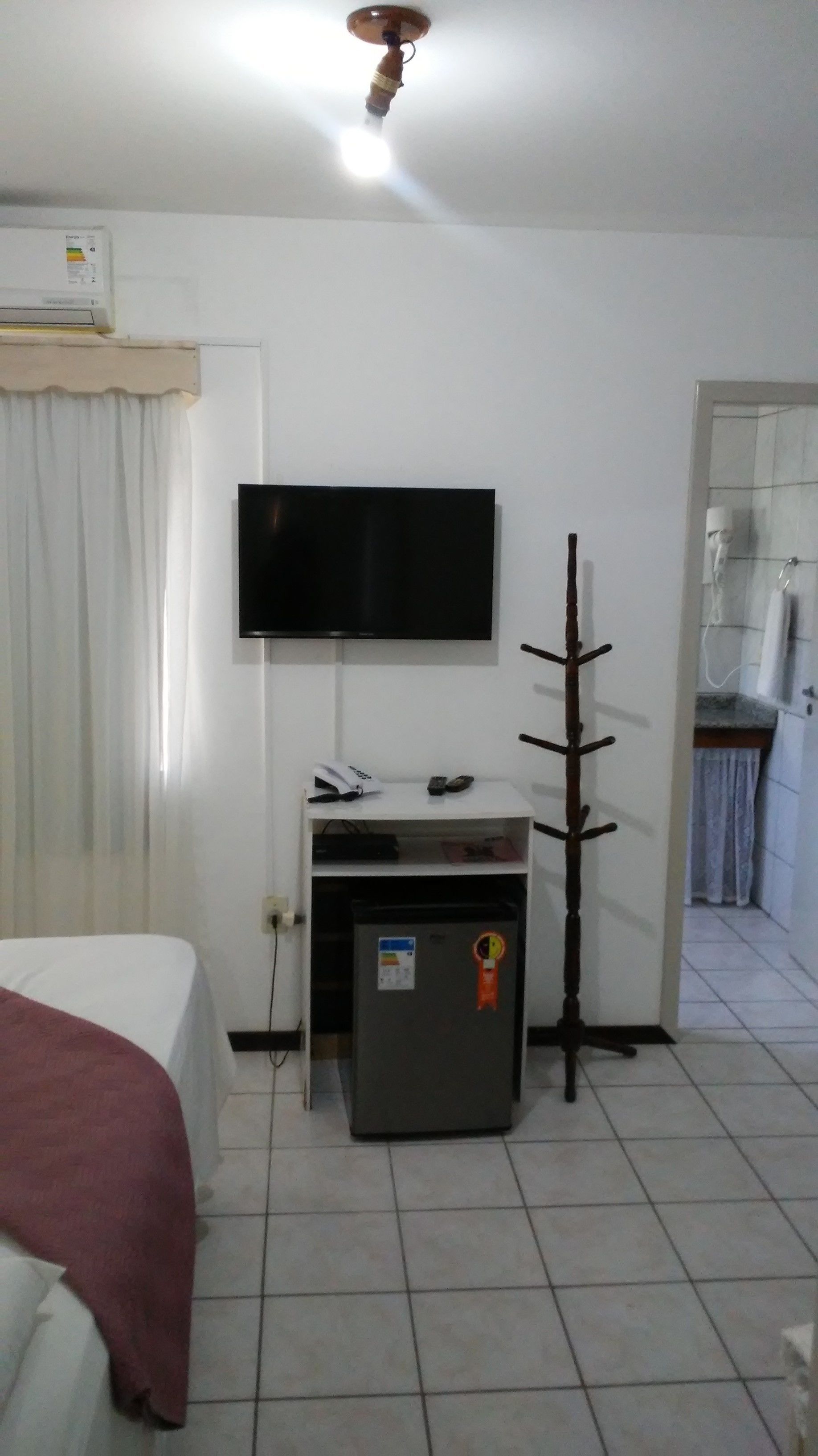 Habitación de hotel con una cama, un televisor montado en la pared, un refrigerador pequeño y una puerta que da al baño.